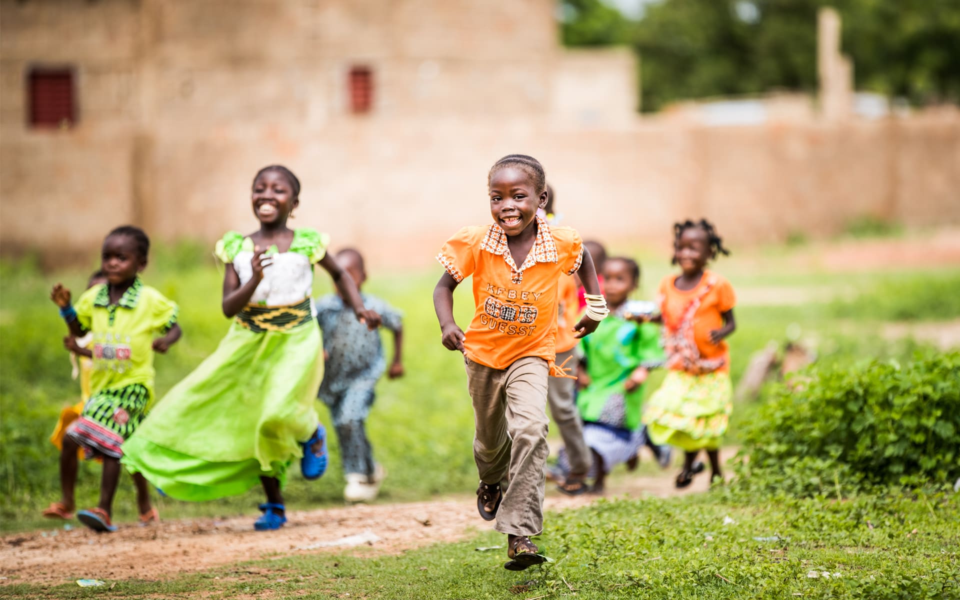 A group of children run on grass towards the camera